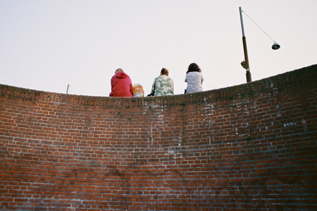 Backs of three woman sitting on red brick wall
